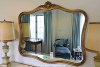 Full view of mirror on wall reflecting room, shows overall shape, gold finish and approximate size.