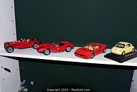 Four model cars displayed on two shelves: two on each shelf against a dark green background