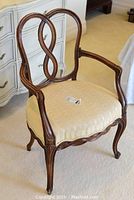 Full side view of the wooden side chair with upholstered cream seat and decorative double-loop backrest, shown on carpeted floor near white dresser.