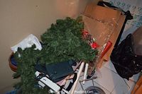 Pile including artificial evergreen wreath and white metal folding luggage rack