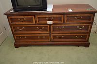 Front view of the wood dresser showing nine drawers with brass handles and a TV placed on top.
