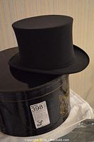 Black top hat resting on its black round storage box with gold decorative design.