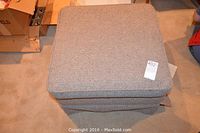 Top view of the square upholstered ottoman showing fabric texture and wear.