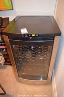 GE Profile wine cooler closed, showing stainless steel frame, glass door, digital panel; telephone visible on left