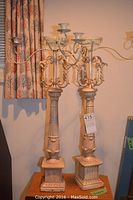 Pair of large antique style metal candelabras standing on wooden table with visible paint damage and chipping.