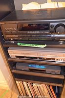 Technics SA-AX710 receiver on top shelf, with two DVD players on shelves below, and vinyl records visible below.