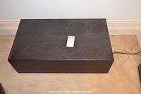 Top view of black rectangular subwoofer with a wood-like exterior surface showing some wear.