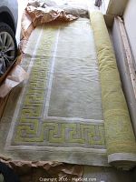 Partial view of the rolled green and beige rug with Greek key border