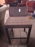Front view of single bar stool showcasing square shape, metal legs in black finish, and brown textured woven plastic upholstery on seat and backrest.