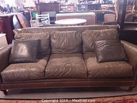 Front view of curved green distressed leather sofa with seat cushions and pillows.