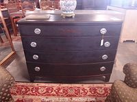 Front view of the dark wood dresser showing four curved drawers with silver metal pulls and reddish floral decoration on top drawer.
