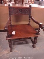 Front view of vintage solid wood armchair highlighting barley twist legs and arms, carved floral and scroll design on backrest.