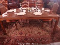 Photo showing the full rectangular solid wood dining table with chairs around it, dark walnut finish, placed on area rugs.