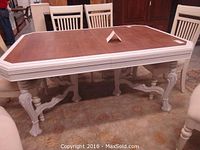 Full view of the dining table showing dark wood top with white painted edges and six intricately carved legs with claw feet.