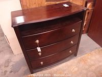 Front view of the curved three drawer dresser showing the dark wood finish and silver metal knobs.