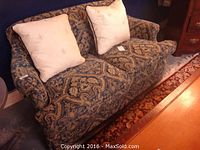 Front view of the designer upholstered loveseat with two cream silk embroidered pillows placed on seat backs.