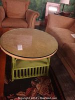 Full view of round glass top coffee table with green painted rattan base and two upholstered chairs around it.