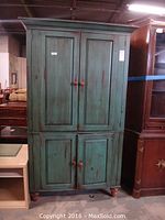 Front view of green shabby chic Romweber entertainment center with four doors and round wooden knobs, standing on short feet.