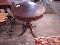 Full view of large circular pedestal table with two drawers and carved legs.