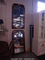 Photo showing both arched wood framed mirrors leaning against the wall in a room with other furniture items.
