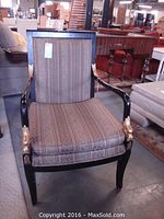 Full frontal view of armchair showing patterned cushion and black wood frame with gold decorative accents on upper armrest and lower arm support near the legs.