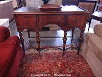 Full front view of the mahogany sideboard showing three drawers, turned legs, and wood finish on a patterned rug between couches.