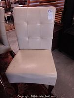 Front view of a white dining chair showing padded tufted back and seat with wooden legs