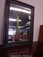 Full view of the rectangular black framed beveled glass mirror, showing reflection of the room.