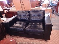 Full view of black loveseat in a room with other furniture, showing its size and style.