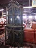 Full front view of two-piece cabinet showing green paint, gold carvings, glass doors