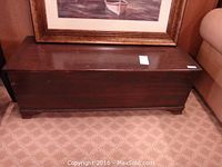 Closed cedar trunk showing dark stained wood exterior with minor surface wear and slightly rounded base edges.