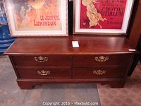 Front view of Lane cedar trunk showing four drawers with brass handles and framed pictures on top.