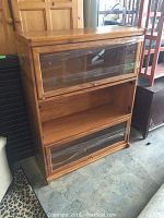 Full view of wooden flip-up cabinet showing three vertical compartments with glass doors on top and bottom, middle open shelf, wood natural finish, glass door missing on bottom compartment