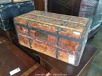 Side view of antique wooden steamer trunk showing wood chipping and metal bands.