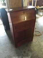 Front view of wooden drop down desk showing closed drop down panel and cabinet door.