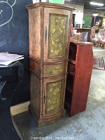 Full view of the wooden corner cabinet showing top door, drawer, and bottom door with floral pattern.