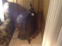 Side view of black cast iron pot belly stove beside floral patterned couch and wood paneled wall.