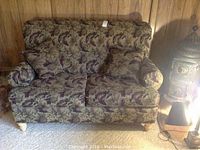 Full view of the floral fabric loveseat in green and eggplant colors, showing overall condition and style.