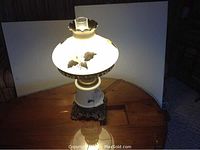 Full lamp lit showing the hand painted lily design on the shade and lamp base, brass base, and glass chimney visible.