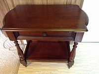 Front view of wooden hall table showing top surface, drawer front, and lower shelf, standing on carpet.