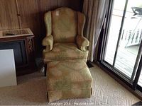 Full view of wing-back chair with ottoman in front of sliding door and wood‐panel wall