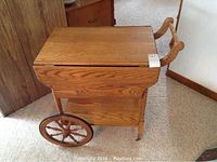 Front-side view of oak tea wagon with leaves closed, spoked wheels and handle