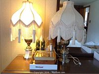 Two brass-look table lamps with fabric fringe shades on wooden surface
