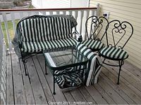 Overall view of the patio set on wooden deck including settee with cushions, two chairs, table, extra cushions, and cover.