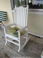 Front-side view of white composite rocking chair with leaf-print seat cushion on wooden porch