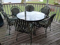 Full lot on porch: round glass-top table, six chairs with striped cushions, cover folded at railing