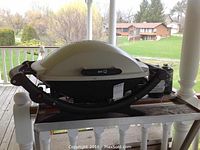 Full side view of the Weber BBQ placed on wooden surface outdoors, showing fold-out sides and propane canister holder.