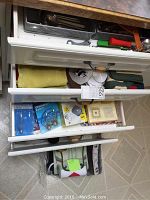 Three kitchen drawers open showing various kitchen items including baking tools, kitchen linens, light bulbs and miscellaneous utensils.