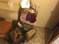 Bathroom lot showing glass and metal shelving with folded towels, decorative box, soap dish, framed prints leaning on floor, toilet paper holder and scale near a toilet.