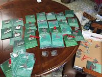 Overhead view of approximately 20 green cards each bearing a pewter building ornament with red ribbon, plus two round medallions at bottom